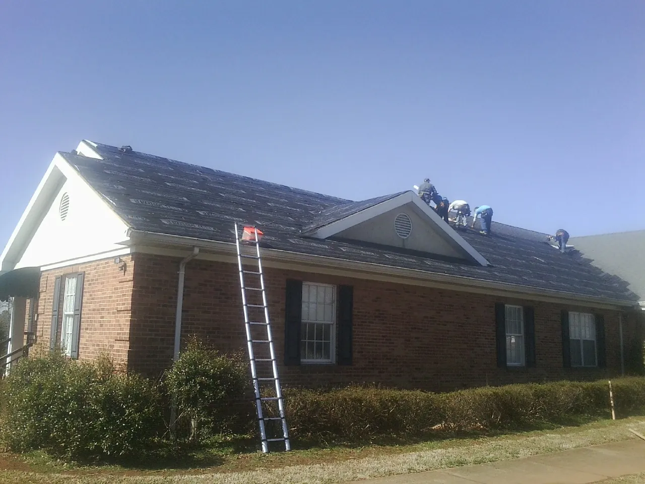 Crew tearing shingles off a brick ranch roof with a ladder set — Emergency Roof Repair work by our crew in Gardnerville
