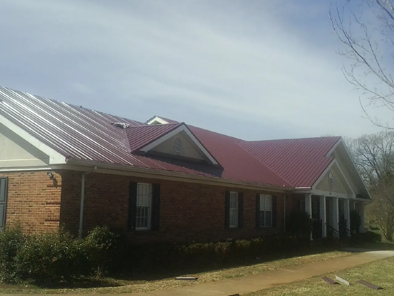 Red metal roof with gabled entries on a long brick building, from a Hail Damage Roof Repair job in Gardnerville