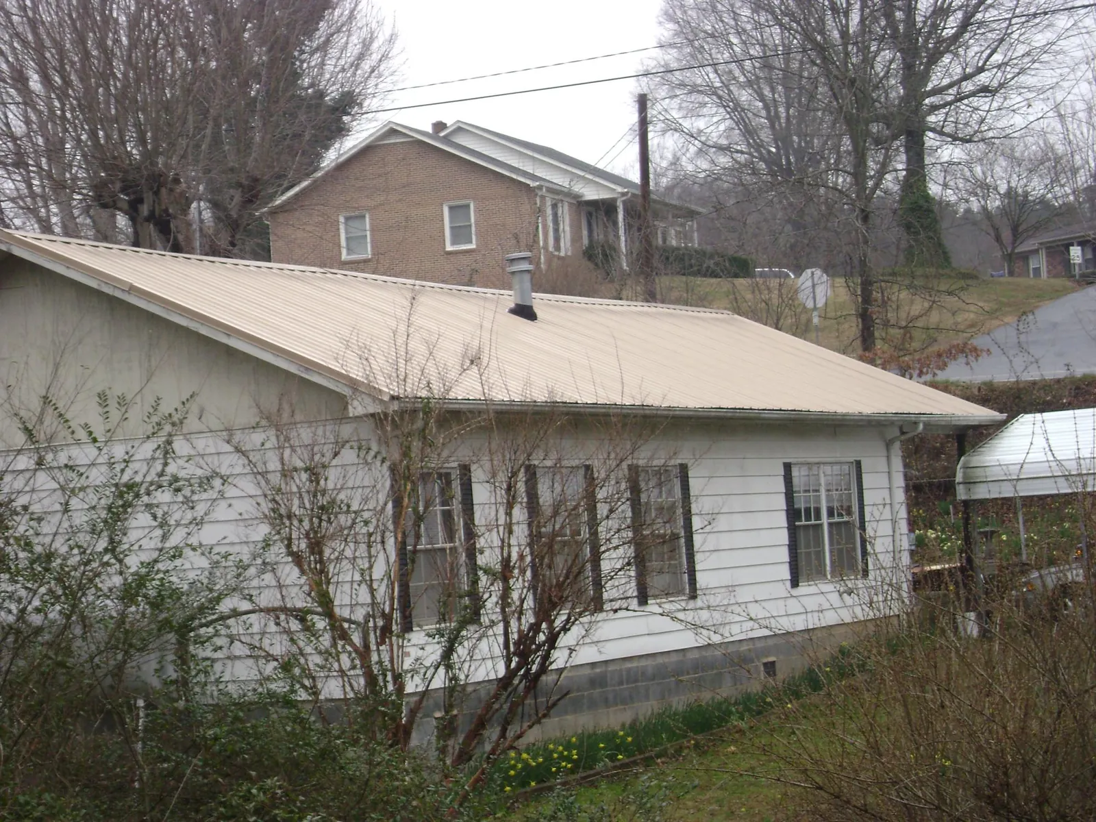 Tan metal roof on a white sided house set into a hillside — Commercial Roofing by Roofing Brothers in Gardnerville